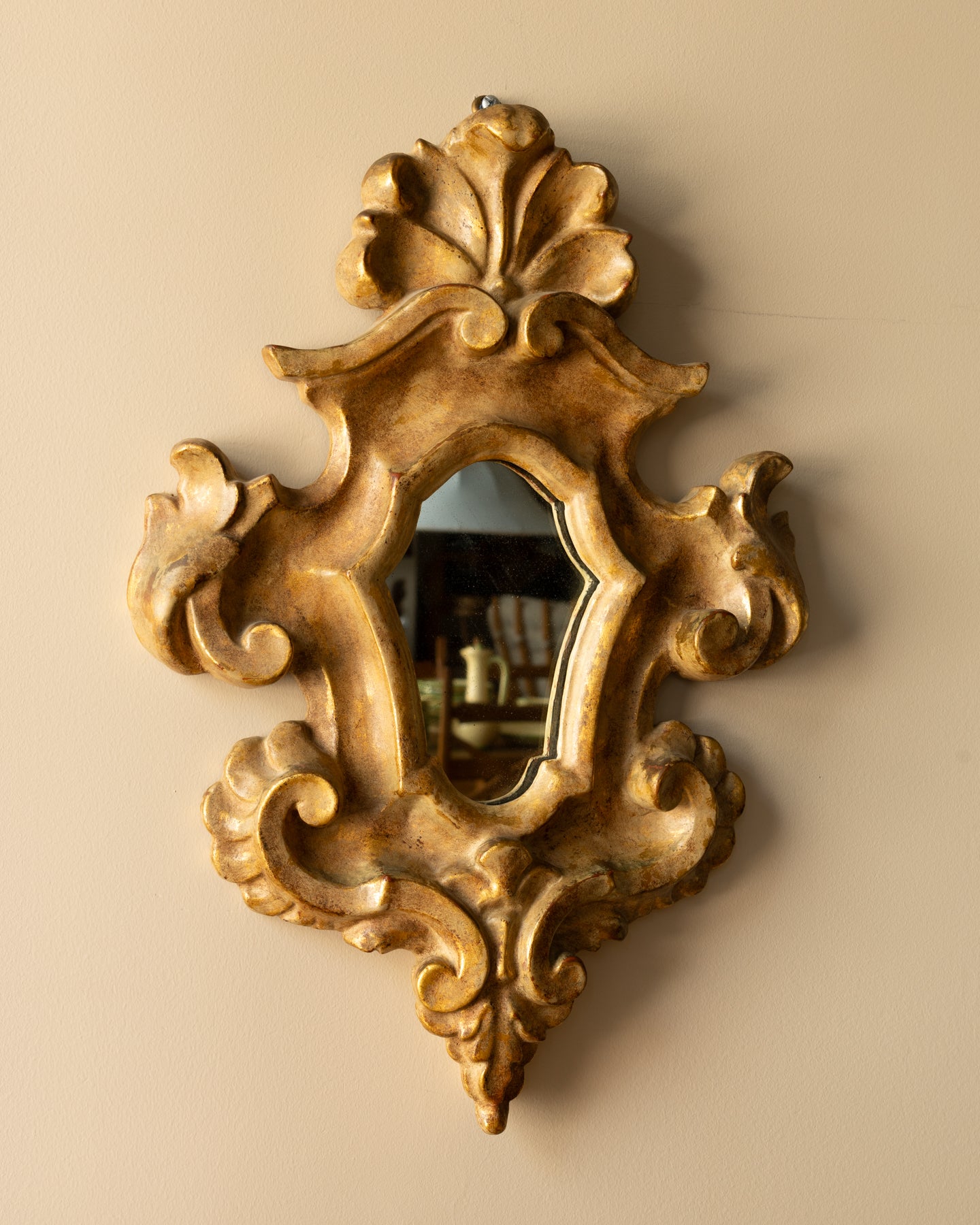 Italian Rococo-style giltwood mirror with curling scrollwork and acanthus carving, aged gold finish, and softly patinated mirror plate; 14″ × 20″.
