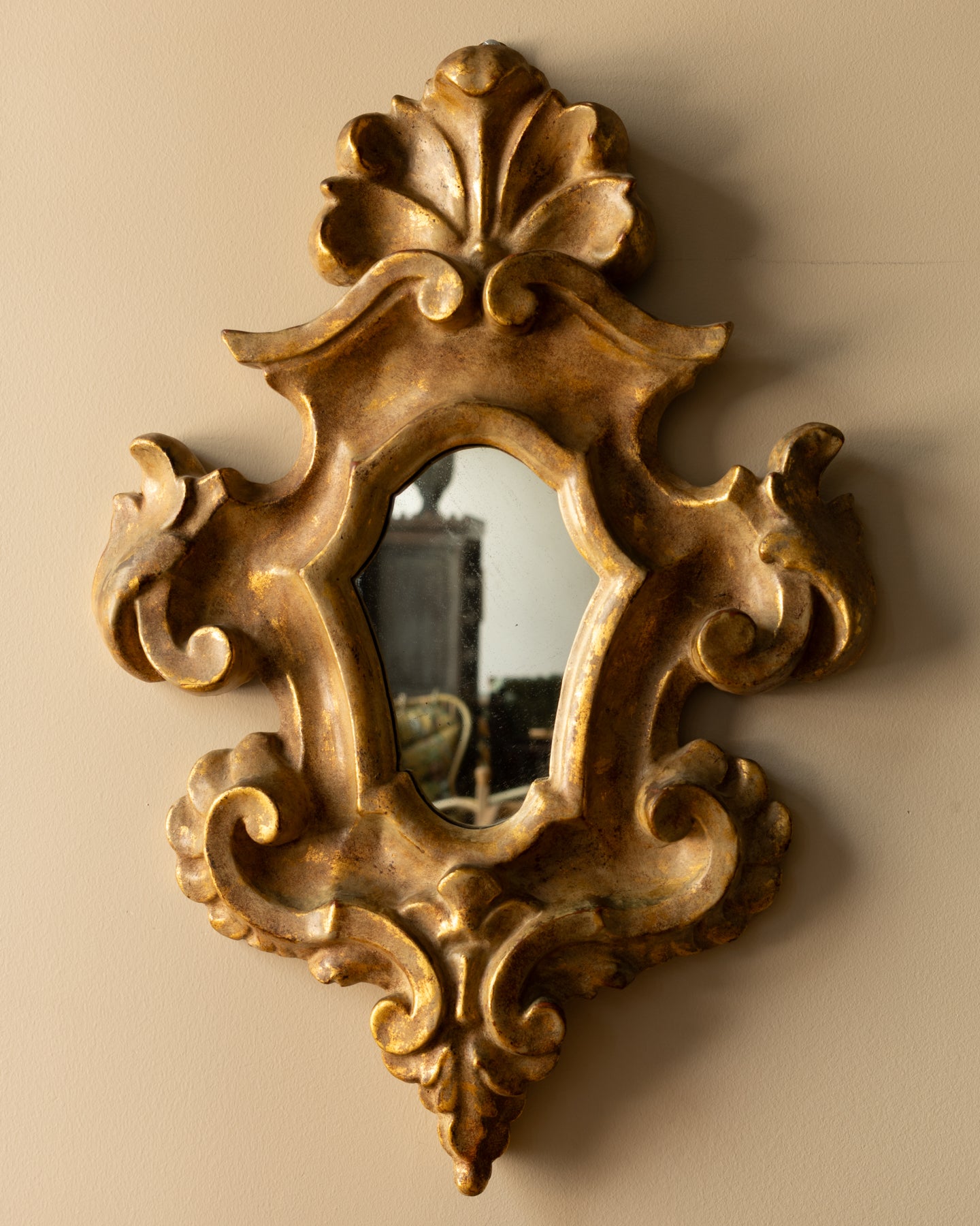 Italian Rococo-style giltwood mirror with curling scrollwork and acanthus carving, aged gold finish, and softly patinated mirror plate; 14″ × 20″.