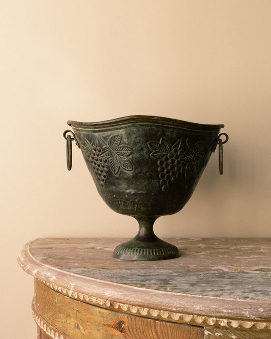 Vintage verdigris cast-metal urn with grape-and-leaf relief and pedestal base.